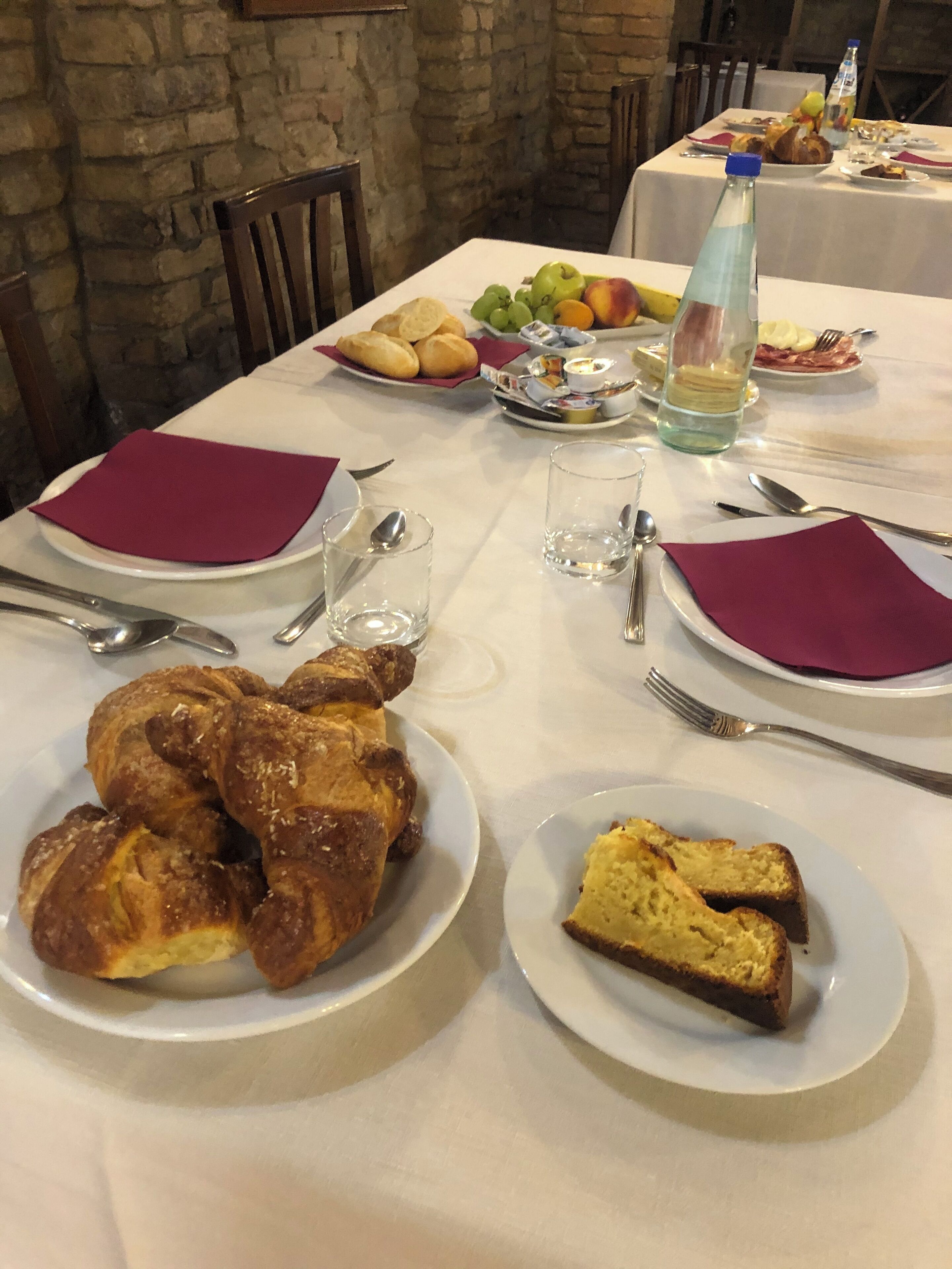 Una mesa de comedor dispuesta con platos de comida, incluyendo un pollo asado grande, pan y una porción de pastel. También hay vasos, cubiertos y una botella de agua sobre la mesa.