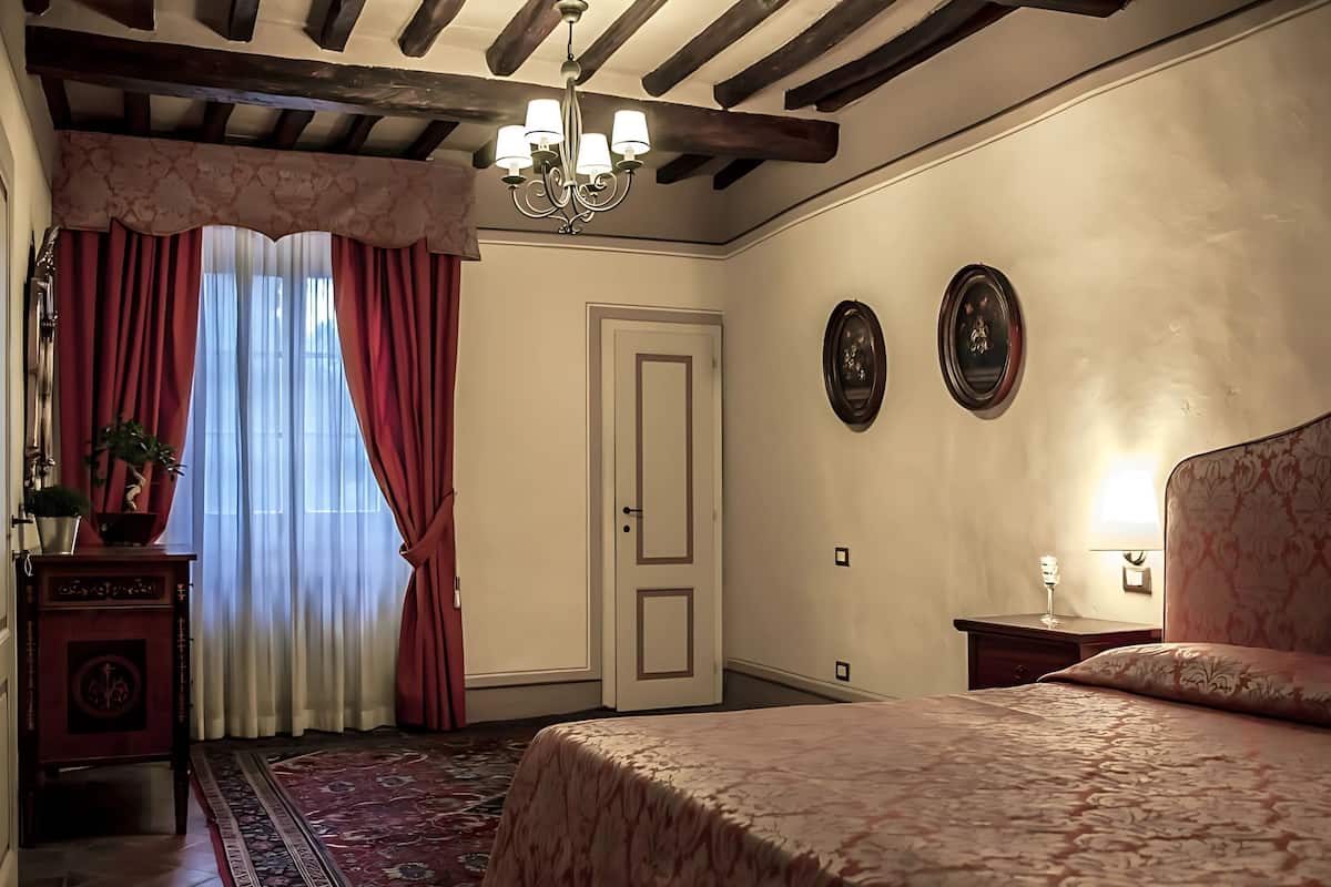 A bedroom with a bed, a chandelier, a door, and a wall with two framed pictures.