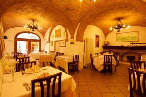 Un ristorante con diversi tavoli, sedie in legno e soffitto in mattoni.