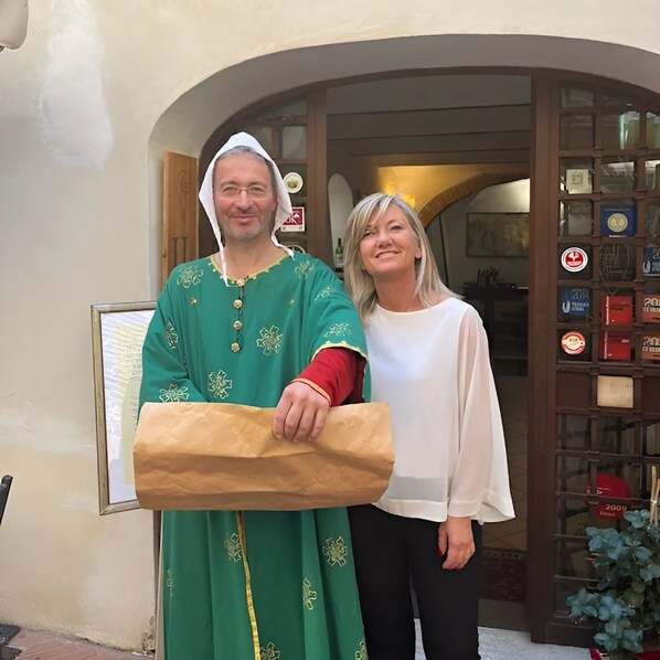 Two people standing in front of a building with a signboard and a display of various items. - Locanda Il Pino (San Gimignano)
