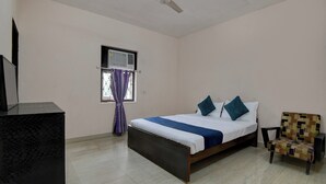 A bedroom with a bed, a chair, a ceiling fan, a window with curtains, and a television on a stand. - Hotel Soft Petal (Bidhannagar)