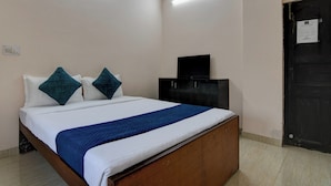A hotel room with a wooden bed, a flat-screen TV on a black cabinet, and a door with a notice on it. - Hotel Soft Petal (Bidhannagar)