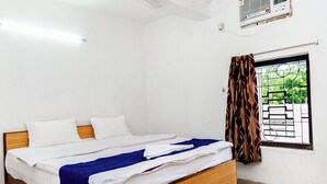 A single-bed room with a wooden frame, white bedding, a blue blanket, and a window with a metal grill and curtains. - Hotel Soft Petal (Bidhannagar)