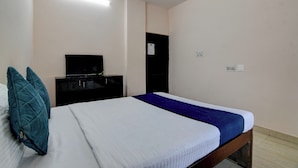 A bedroom with a bed, a dresser, a television, and a door. - Hotel Soft Petal (Bidhannagar)