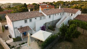 Un bâtiment blanc avec un toit recouvert de tuiles, un escalier et un patio aménagé avec des chaises et un parasol.