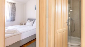 Une chambre d’hôtel avec un lit, une table de chevet, une douche et une armoire en bois.