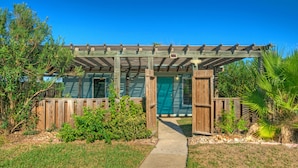 Une pergola en bois avec un chemin menant à un bâtiment doté d’une porte verte.