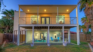 Ein zweistöckiges Haus mit überdachter Terrasse, Gartenmöbeln und umzäuntem Grundstück.