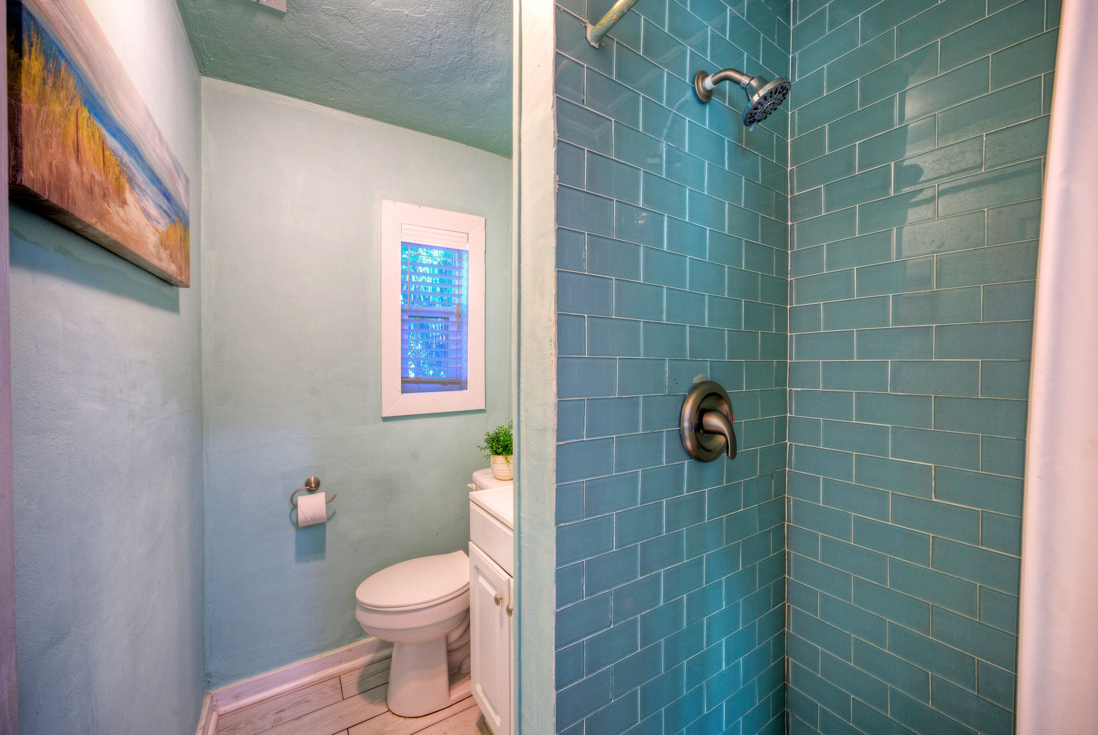 Ein Badezimmer mit Duschkabine mit blauen Fliesen, Toilette und einem gerahmten Bild an der Wand.