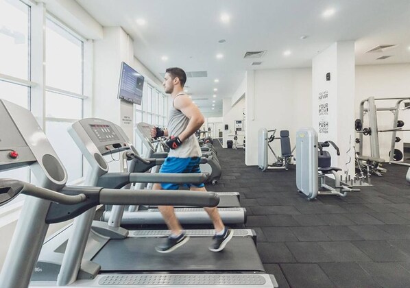 A gym with treadmills, weight machines, and a TV screen.