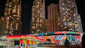 A brightly lit gas station with a colorful mural, surrounded by tall residential buildings at night. - Luxury 19th Floor Condo with Pool, Gym & City View (Skopje)