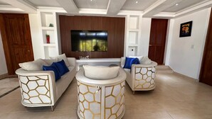 A modern living room with a large flat-screen TV, two white sofas with geometric patterns, a central coffee table, and a wooden door. - 3-bedroom villa in tranquil Cap Cana Punta Cana with AC (Cap cana punta cana)