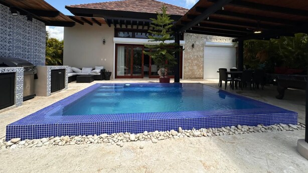 A rectangular swimming pool with blue tiles, surrounded by a pebble border, under a covered patio area. - 3-bedroom villa in tranquil Cap Cana Punta Cana with AC (Cap cana punta cana)