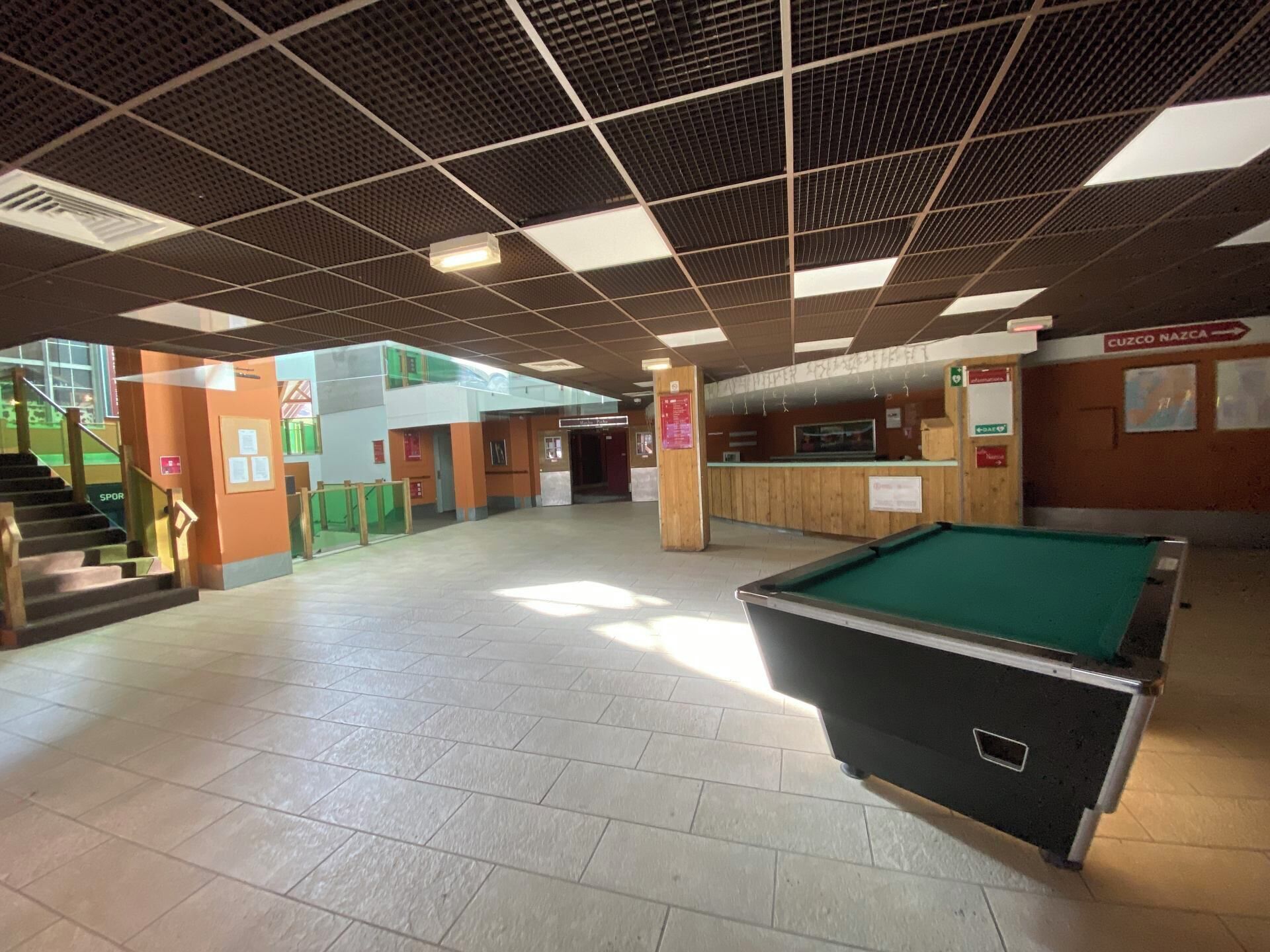 Un grand espace intérieur comprenant une table de billard, un escalier et un comptoir d’accueil.