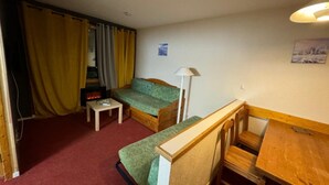 Une pièce de taille modeste, avec un canapé vert, une petite table, un bureau en bois et une lampe.
