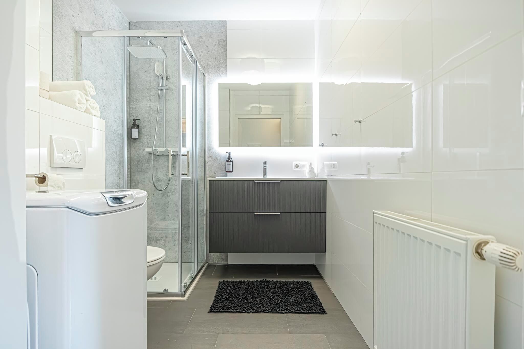 Une salle de bain moderne avec une douche à parois de verre, des toilettes, un lavabo avec un miroir et un radiateur.