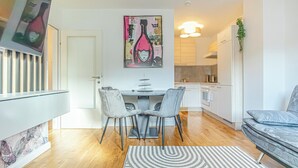 Une cuisine moderne avec des meubles blancs, une table à manger avec deux chaises et un tableau suspendu au-dessus de la table.
