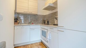 Une cuisine compacte avec des meubles blancs, un four encastré et une machine à café.