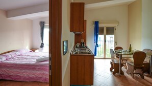 Camera d'albergo compatta con letto, angolo cottura e zona pranzo con sedie e tavolo.