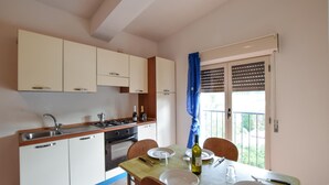 Una cucina compatta con zona pranzo, piano cottura a gas, lavello e finestra con persiane.