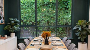 A dining area with a long wooden table set for six, surrounded by grey upholstered chairs. A modern chandelier with spherical glass shades hangs above. - Elwood Retreat - Sauna, 4 bedrooms, large garden, close to shops, cafe, train (Elwood)