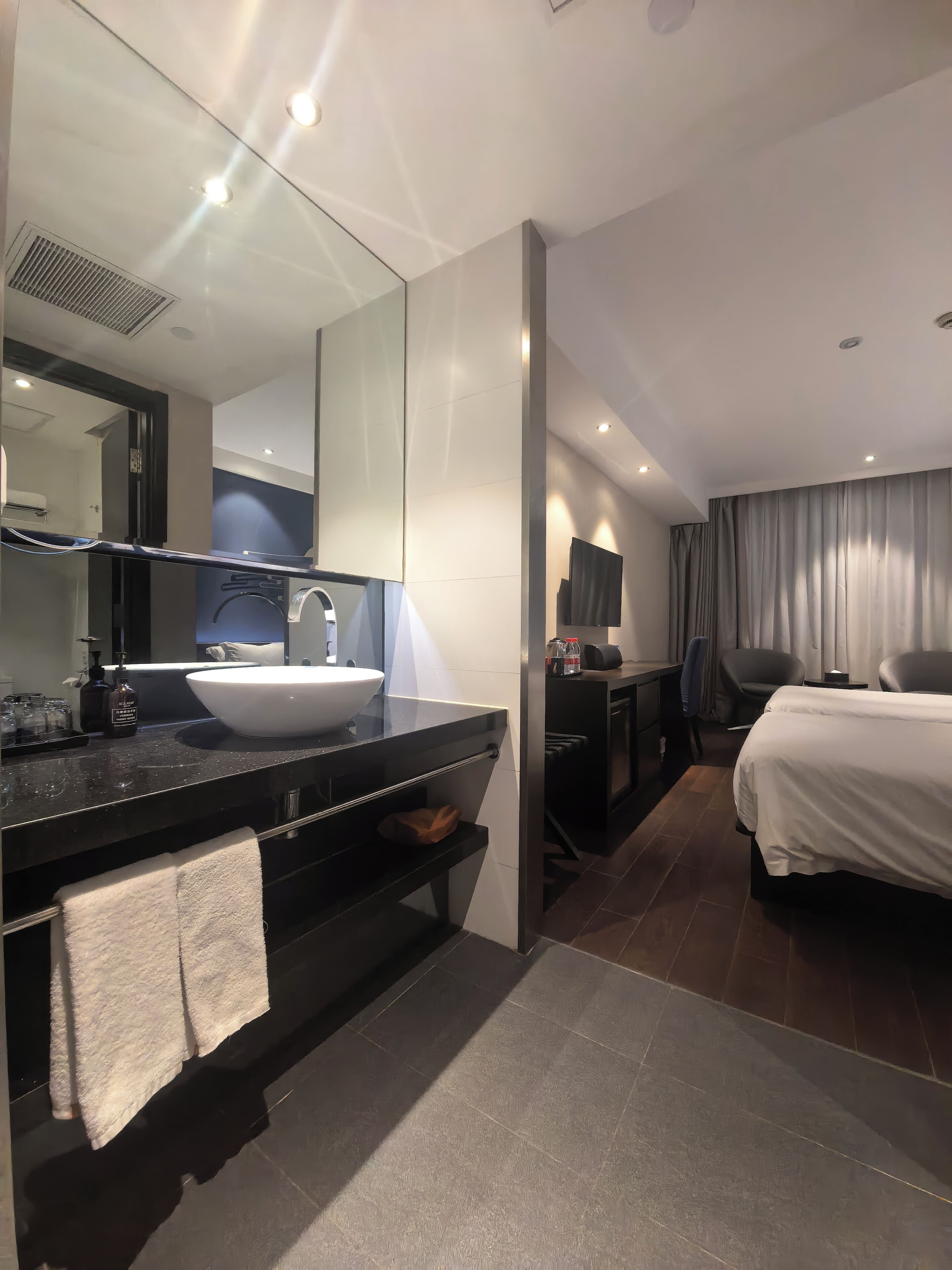 A modern hotel bathroom with a large sink, mirror, and dark countertop.