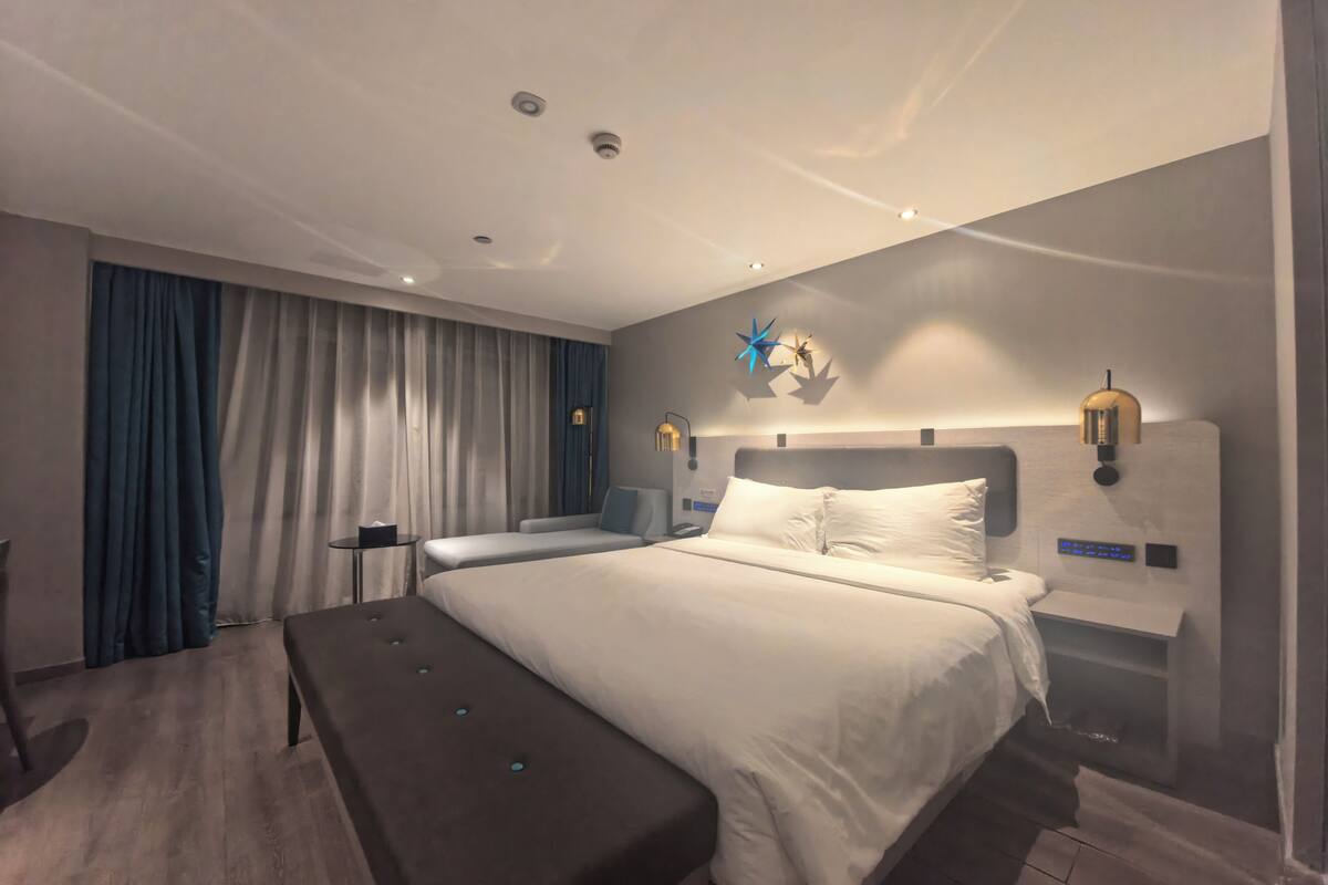 Een moderne hotelkamer met een groot bed, nachtkastjes, een bankje en een bureau.