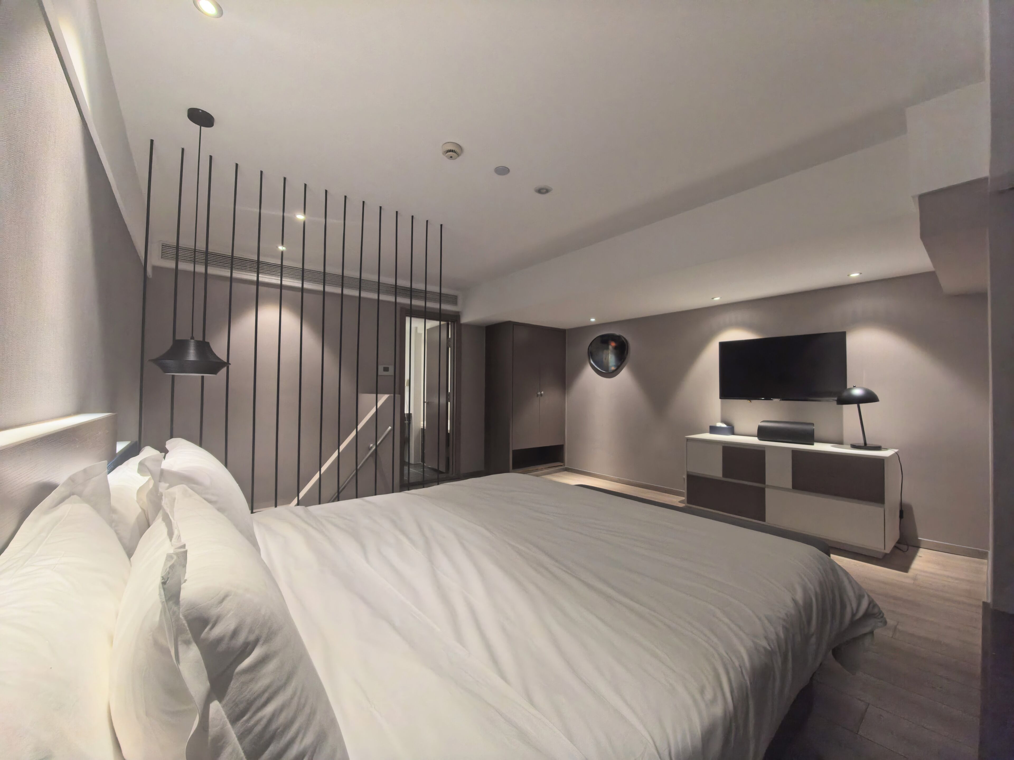 A modern bedroom with a large bed, a TV, and a desk with a lamp.