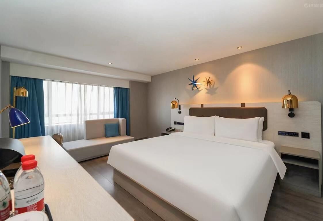 Una habitación de hotel moderna con una cama grande, un escritorio con silla, un sofá y una ventana con cortinas.