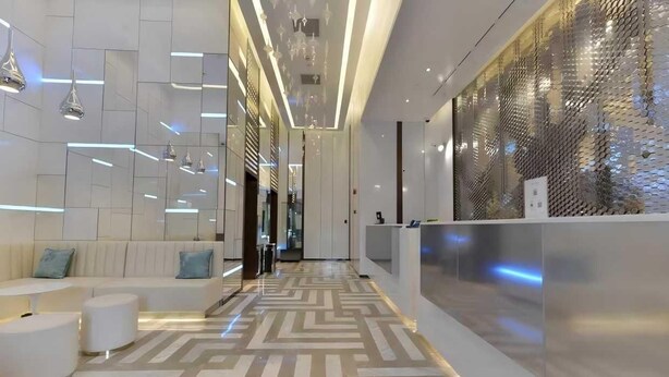Un hall d’entrée moderne avec un sol à motifs géométriques, un comptoir d’accueil et un espace détente comprenant un canapé et des poufs.