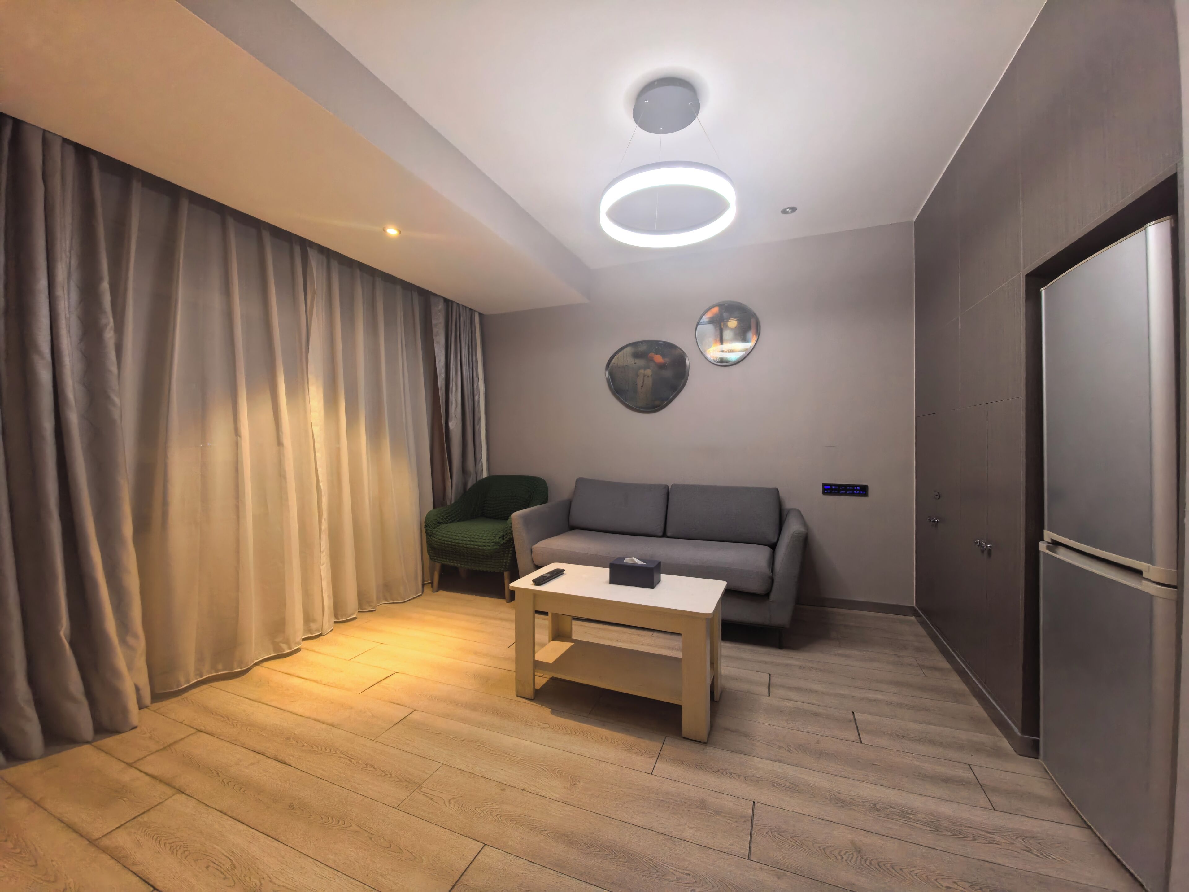 A modern living room with a grey sofa, a wooden coffee table, a green armchair, and a large circular mirror on the wall.