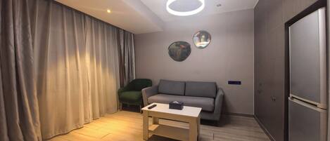 A modern living room with a grey sofa, a wooden coffee table, a green armchair, and a large circular mirror on the wall.