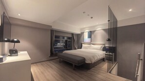 Une chambre d’hôtel moderne avec un grand lit, une table de chevet et une vue sur la ville la nuit.