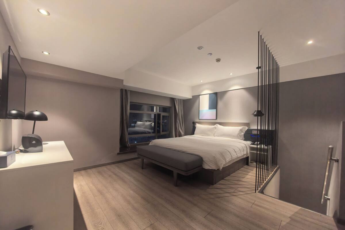 Een moderne hotelkamer met een groot bed, nachtkastje en uitzicht op de stad bij nacht.