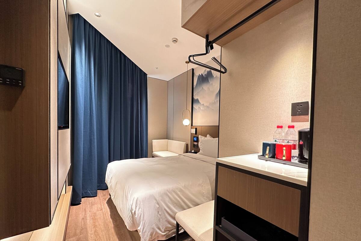 Een hotelkamer met een bed, een bureau met een computer, een stoel, een spiegel en een raam met gordijnen.