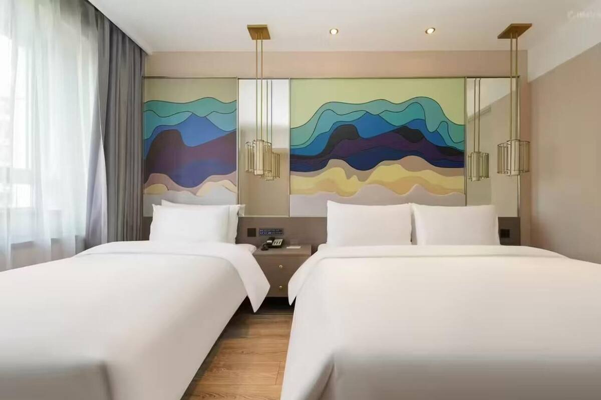 Een hotelkamer met twee bedden, een groot abstract schilderij aan de muur en een moderne kroonluchter.