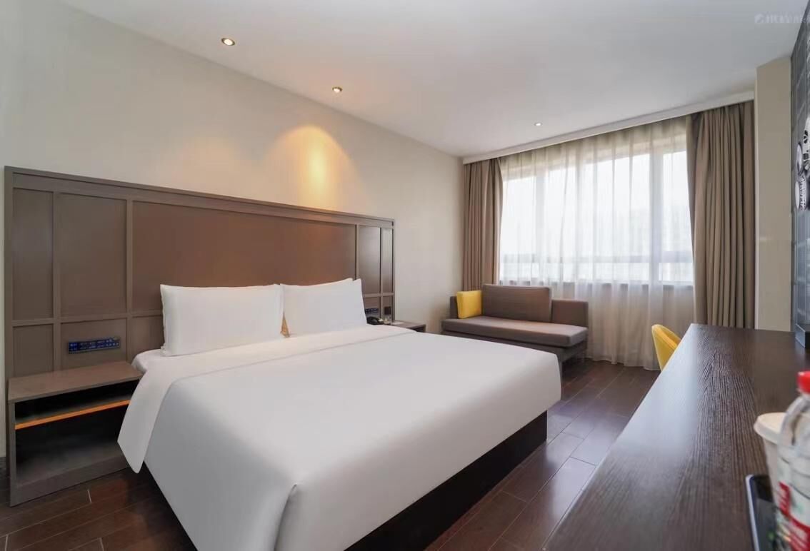 A hotel room with a large bed, a sofa, a desk, and a TV.
