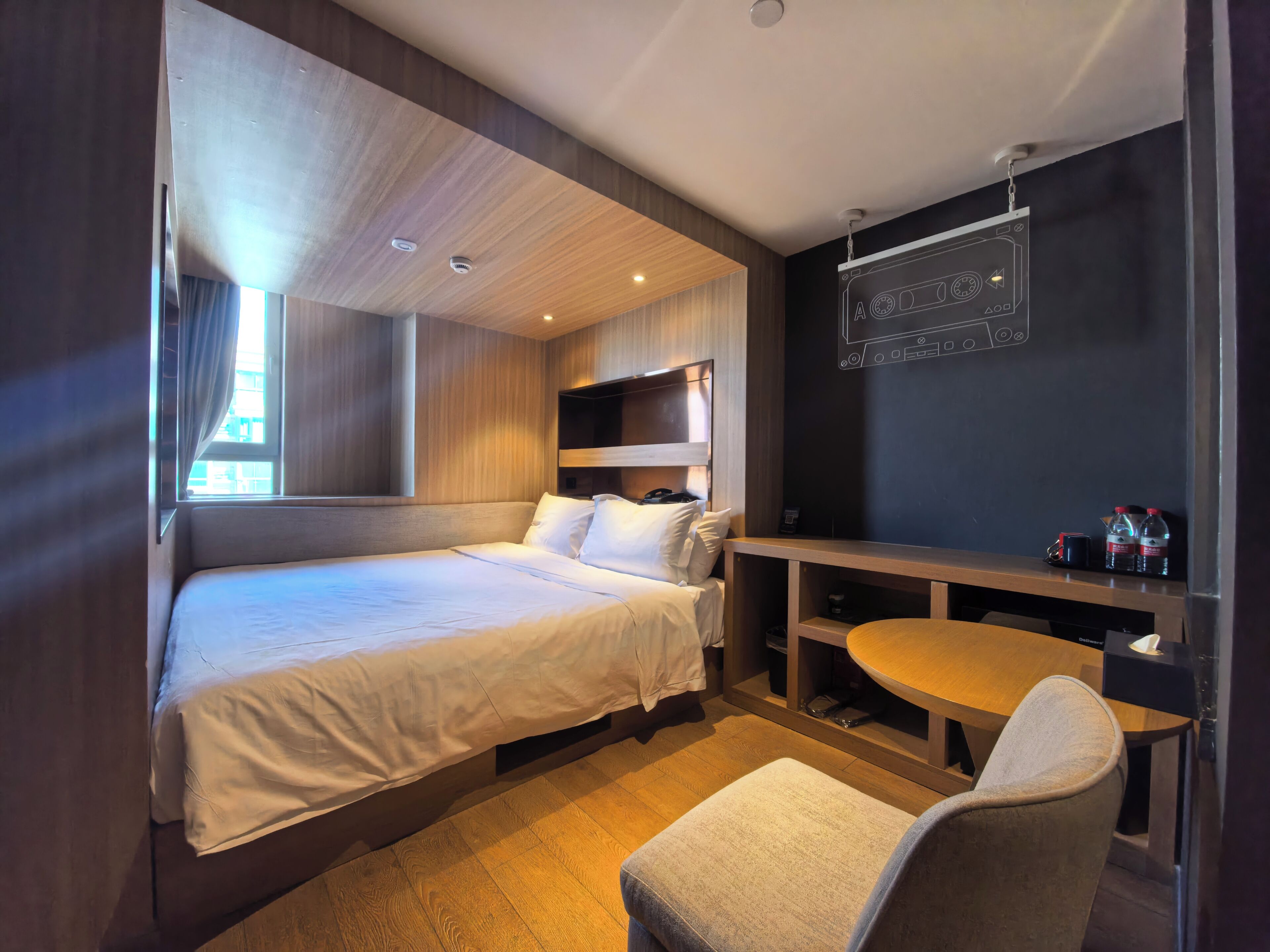 Ein Hotelzimmer mit zwei Betten, einem kleinen Tisch, einem Stuhl und einem an der Wand befestigten Regal mit Gegenständen.