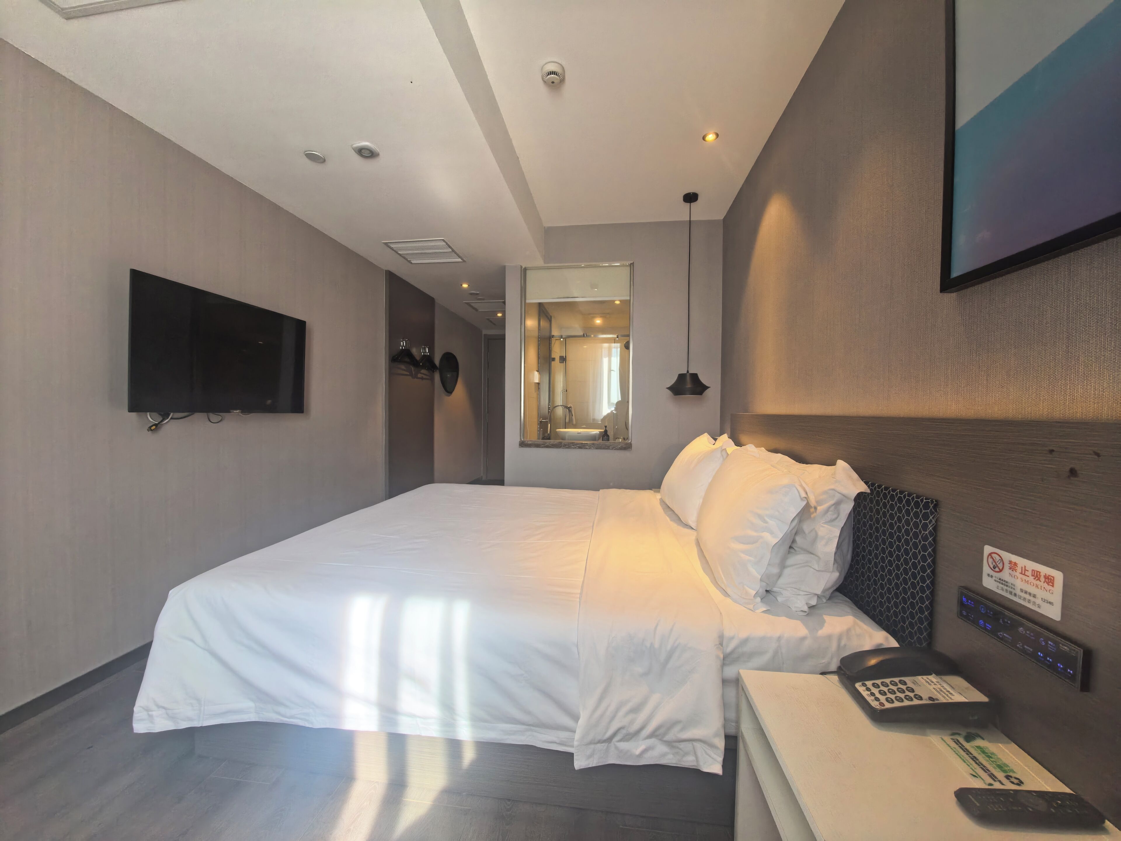 Habitación de hotel con una cama grande, televisión montada, teléfono junto a la cama y un espejo.