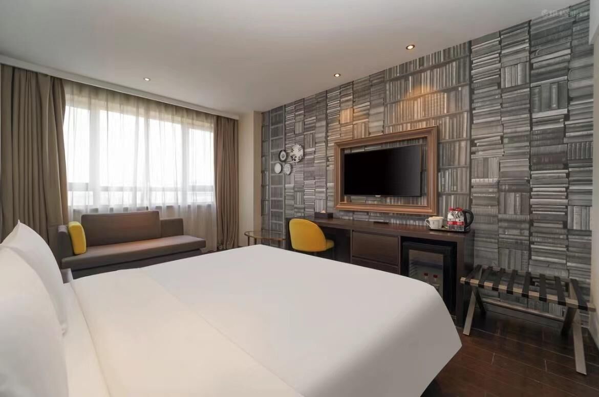 A hotel room with a large bed, a TV, a desk with a chair, and a sofa.