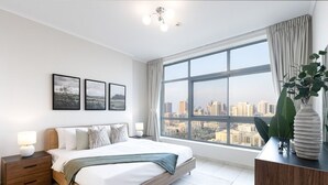 A modern bedroom with a large window, a bed, bedside tables, and framed pictures on the wall. - Modern Retreat in The Views with Balcony & Pool (Dubai)