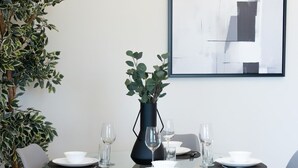 A modern dining area with a round table, two chairs, a vase, and a framed abstract painting on the wall. - Stylish 1BR Retreat with Pool & Stunning City View (Dubai)