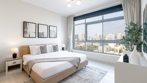 Un dormitorio moderno con una cama grande, mesitas de noche, vistas a la ciudad y un amplio ventanal.