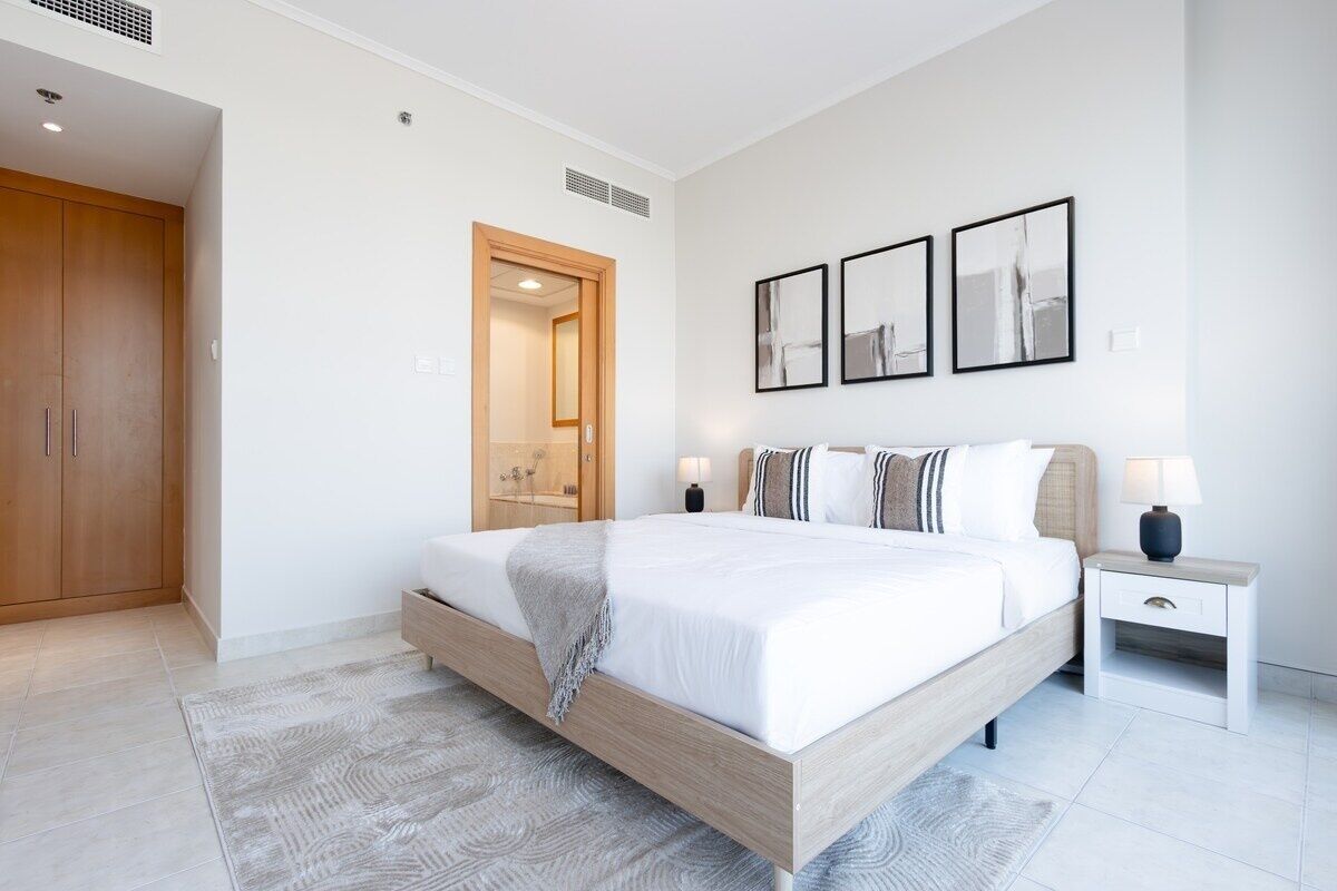 Ein modernes Schlafzimmer mit einem großen Bett, einem Holzschrank, einem Nachttisch mit Lampe und einem gerahmten Kunstwerk an der Wand.