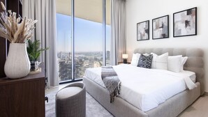 A modern bedroom with a large bed, a view of the city, and abstract art on the wall. - Elegant 1BR in JVC with Pool & Gym (Dubai)