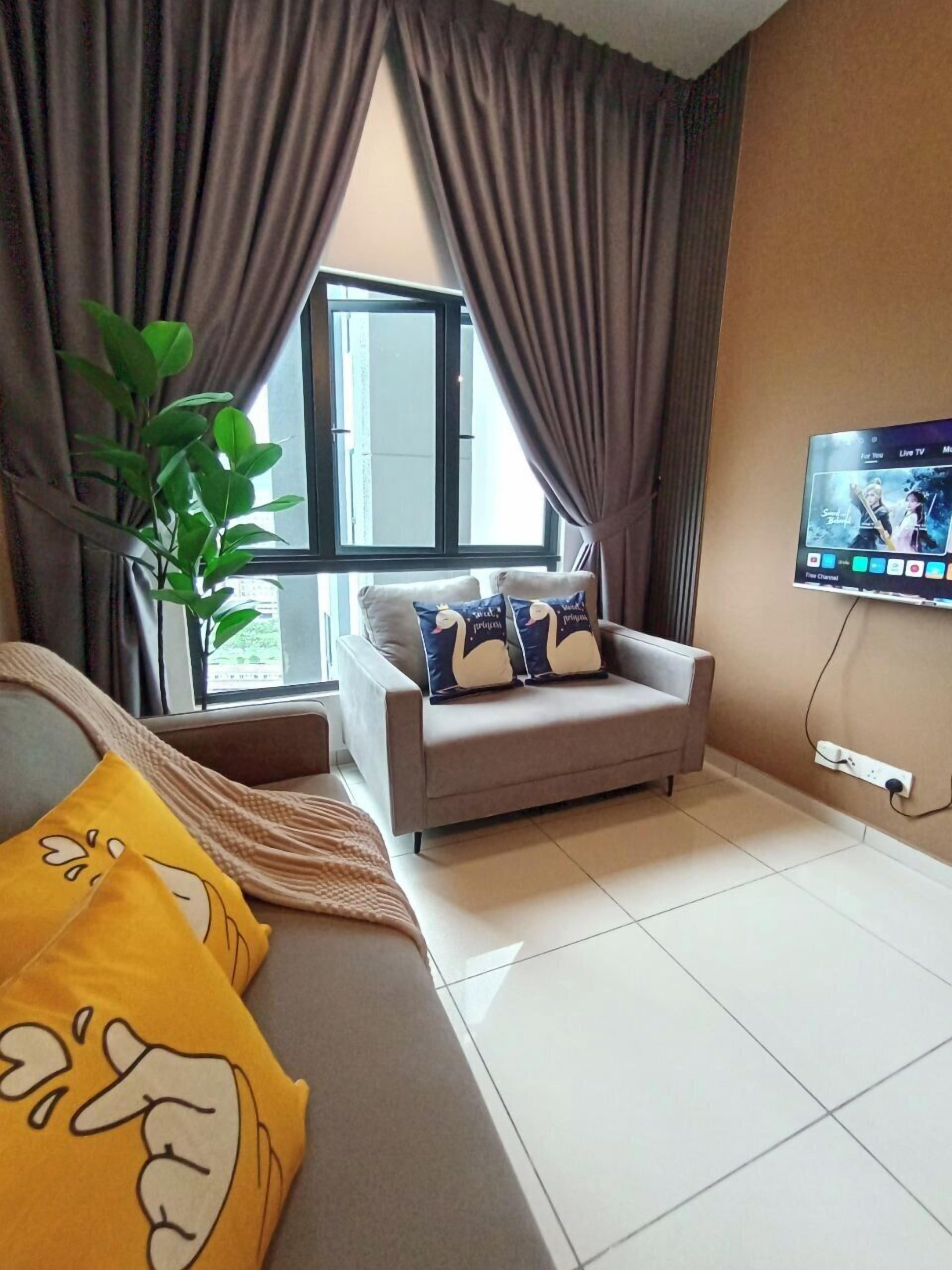 A room with a bed, a sofa, a TV, a window, and a plant.