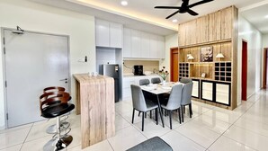 A modern kitchen with white cabinets, a dining area with a round table and chairs, and a bar area with stools. - The Horizon Ipoh Skyline By Grab A Stay (Ipoh)
