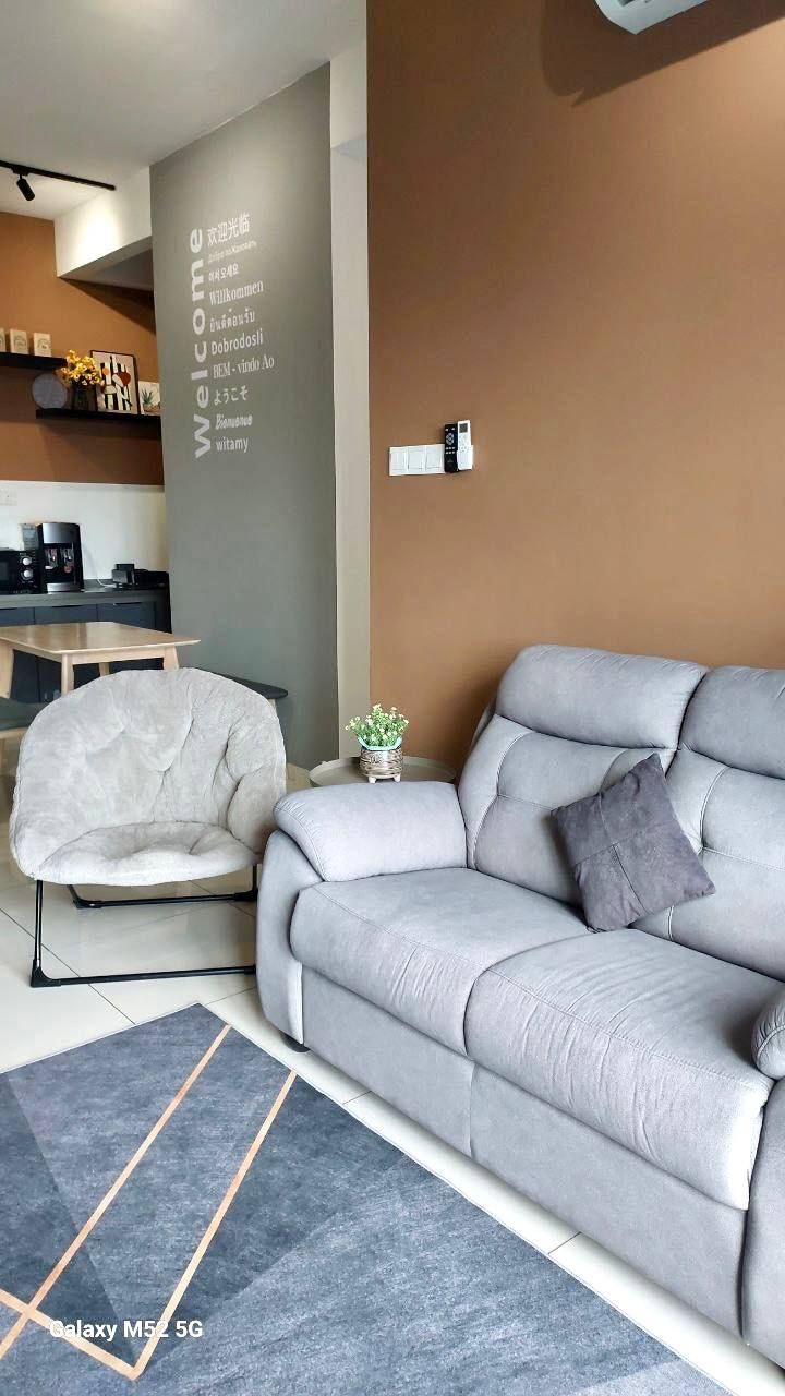 A modern living room with a grey sofa, a white armchair, and a small side table with a plant. A coffee machine is visible in the background.