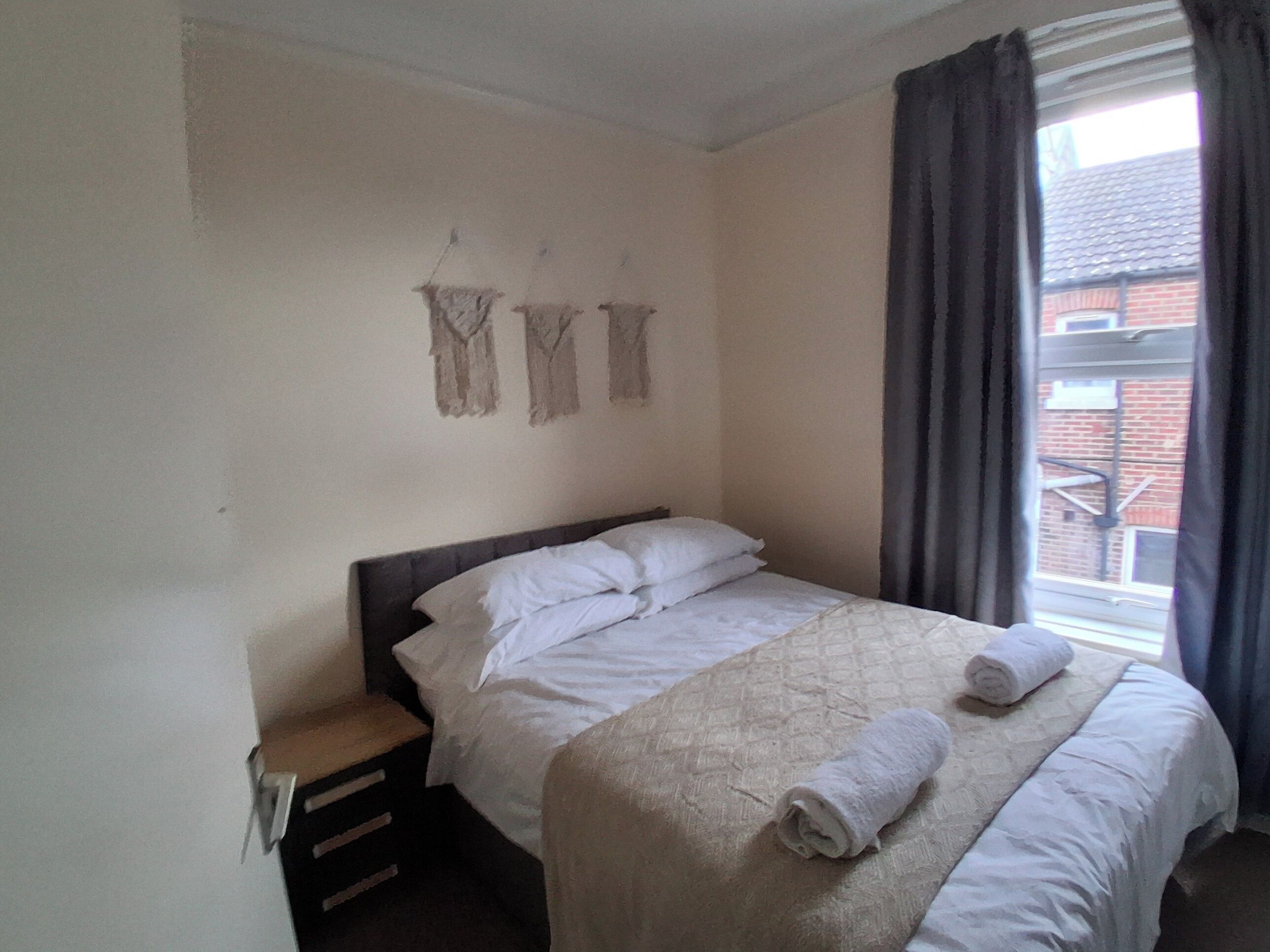 A bedroom with a bed, a nightstand, and a window with curtains.