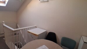 A small, cozy room with a round table, a chair, a radiator, a white desk, and a wall-mounted light fixture. - Southampton Serenity - 3 Bedroom Apartment (Southampton)